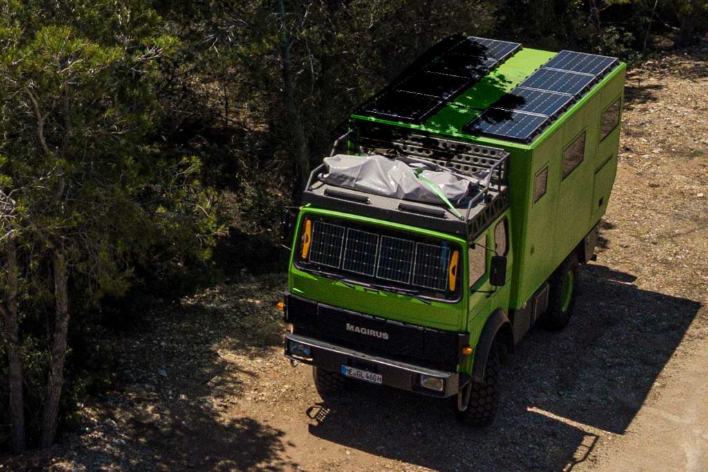 Expeditionsmobil mit Solaranlage im Halbschatten vor Bäumen